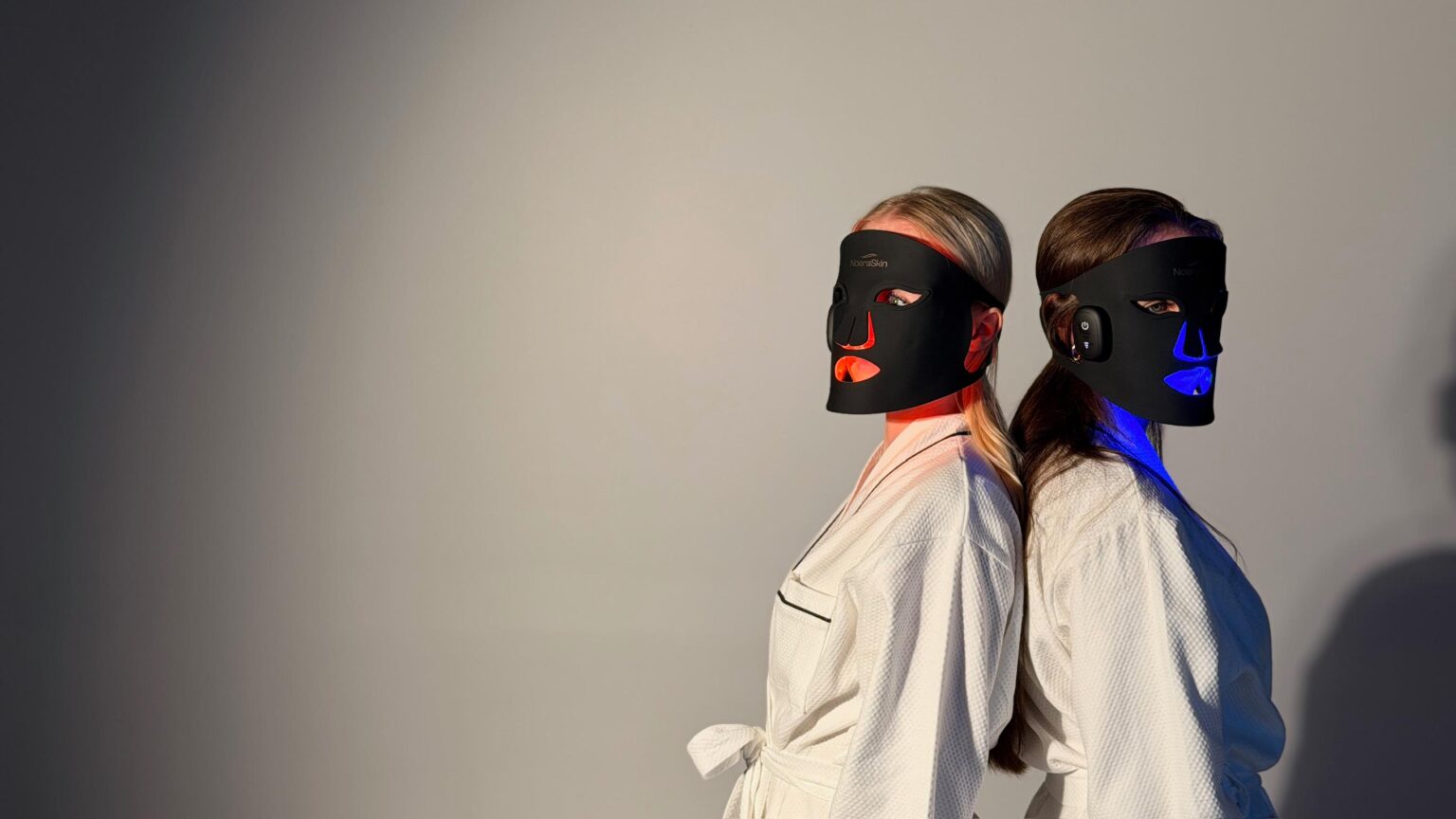Two women wearing the NoeraSkin LED mask, one with red light and the other with blue light