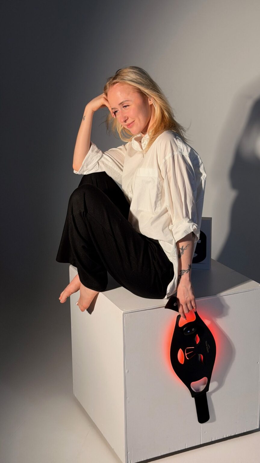 A woman sitting on a white block holding the mask glowing red