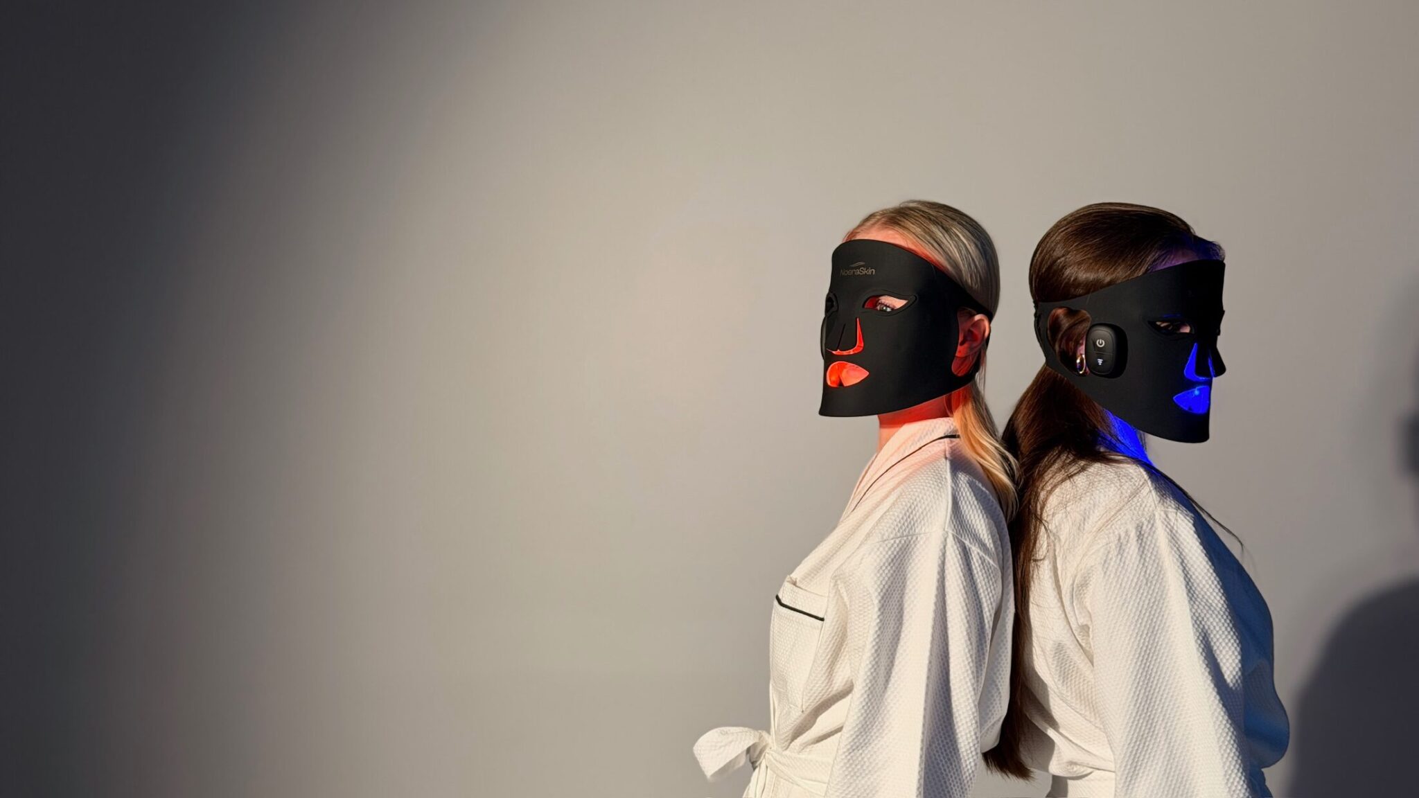 Two women back to back wearing the mask, one lit red, one lit blue